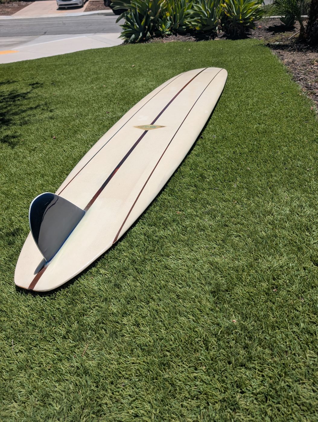 Repaired longboard with a fresh fin lying on grass