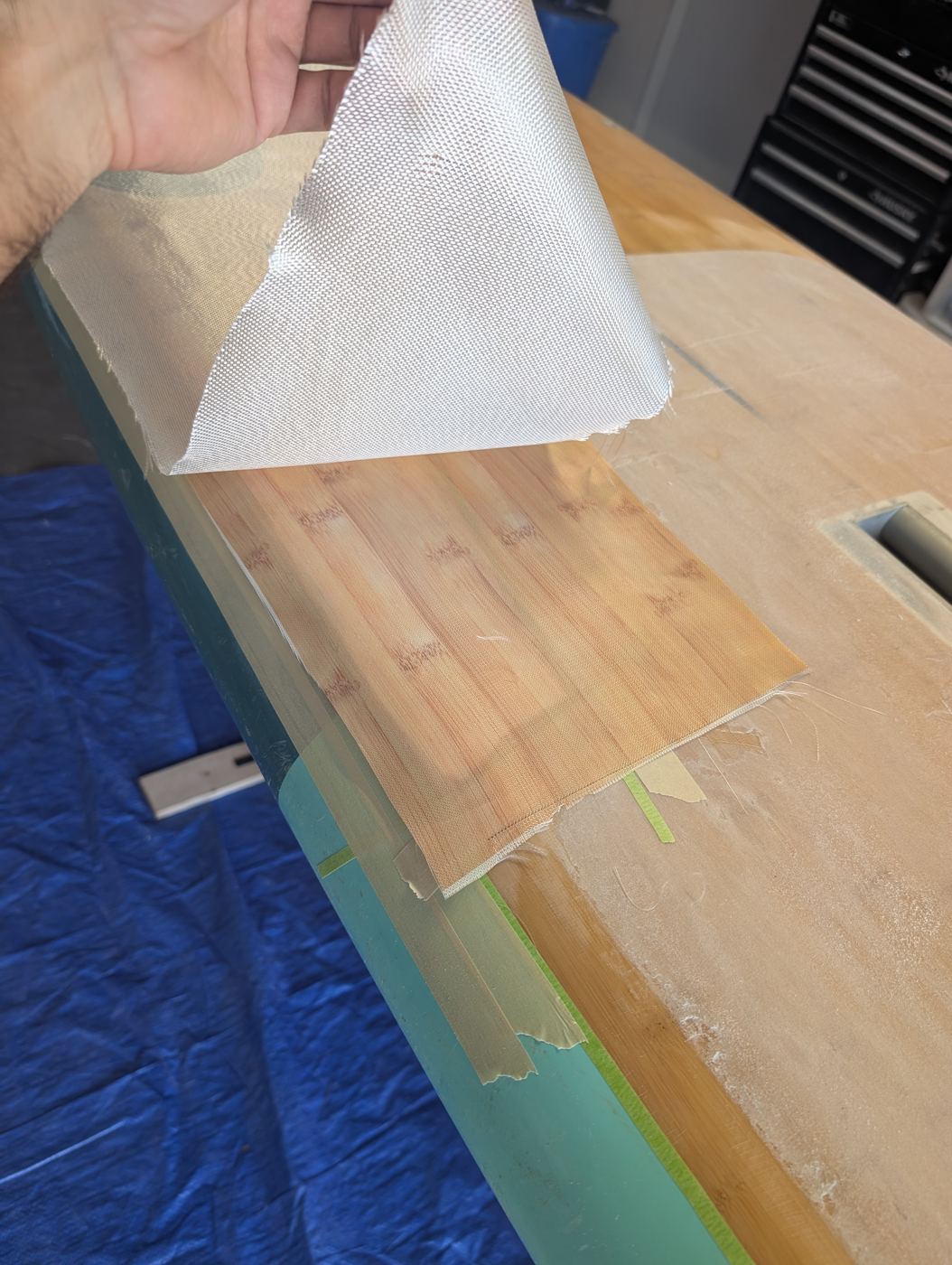 Fiberglass cloth being laid over the repaired area of a bamboo paddleboard